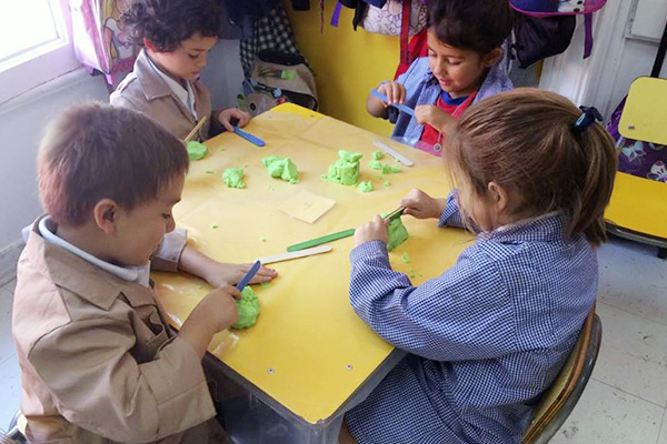 La imagen muestra a niños y niñas en una mesa de trabajo realizando figuras con arena para moldear