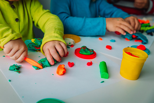 La imagen muestra los brazos de dos niños que están realizando figuras con masas