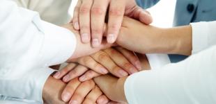 La imagen muestra a varias personas colocando sus manos una sobre otras en señal de colaboración