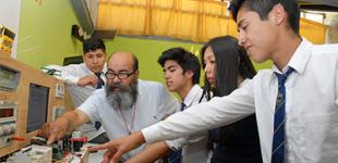 Profesor y sus estudiantes aprendienso sobre circuitos en liceo Técnico Profesional. 