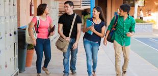 grupo de jóvenes, dos hombres y dos mujeres, que conversan en un pasillo de un establecimiento educacional