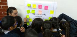 Estudiantes pegan en la pared ideas escritas en una papel