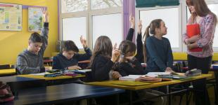 mujer adulta hablando a niños sentados en sus bancos en una sala de clases