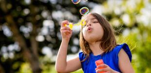 La imagen muestra una niña haciendo burbujas de jabón