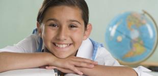 La imagen muestra a una niña sonriente apoyada sobre un libro abierto y un globo terraqueo atrás