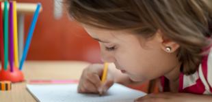 La imagen muestra una niña escribiendo en un cuaderno