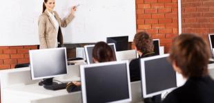 La imagen muestra estudiantes en sala de computadores con profesora entregando contenido