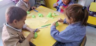 La imagen muestra a niños y niñas en una mesa de trabajo realizando figuras con arena para moldear