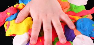 La imagen muestra una mano de niño sobre plasticinas de diversos colores