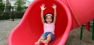 La imagen muestra a una niña en un resbalín en un parque
