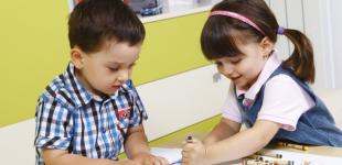 La imagen muestra a una niña y un niño haciendo dibujos juntos en una mesa