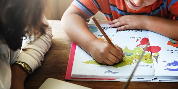 Niño coloreando un mapa mundi junto a su madre.