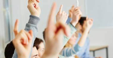 La imagen muestra a estudiantes levantando la mano para pedir la palabra