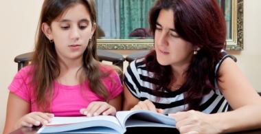 La imagen muestra una madre que lee junto a su hija, ambas sentadas en una mesa