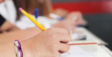 La imagen muestra un estudiante escribiendo en un cuaderno