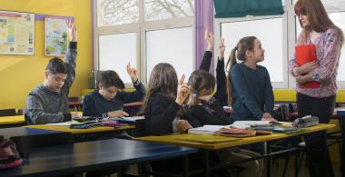 mujer adulta hablando a niños sentados en sus bancos en una sala de clases