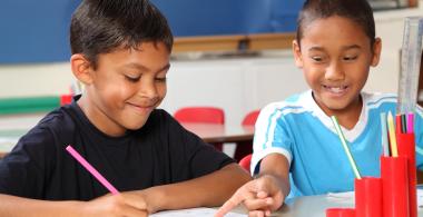 La imagen muestra 2 niños revisando un cuaderno