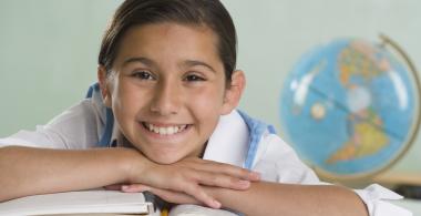 La imagen muestra a una niña sonriente apoyada sobre un libro abierto y un globo terraqueo atrás