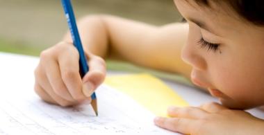 La imagen muestra a un niño escribiendo letras en un cuaderno