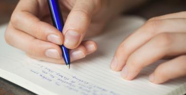 La imagen muestra una persona escribiendo en una libreta