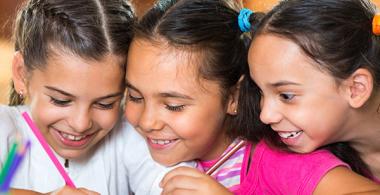 La imagen muestra a 3 niñas realizando actividades en un cuaderno