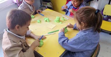 La imagen muestra a niños y niñas en una mesa de trabajo realizando figuras con arena para moldear