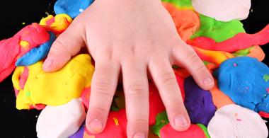 La imagen muestra una mano de niño sobre plasticinas de diversos colores