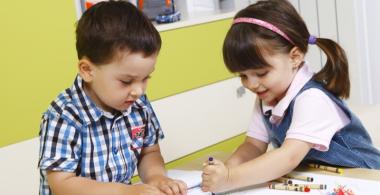 La imagen muestra a una niña y un niño haciendo dibujos juntos en una mesa