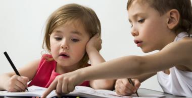 La imagen muestra a una niña y un niño miran contenido en un libro